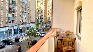 A balcony with a table and chairs, overlooking a street with cars and buildings. - Aperol Apartment - Malaga (Málaga)