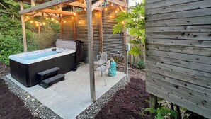 Puinen pergola, jonka alla on poreallas ja jossa on valoketju, ja jonka ympärillä on puutarha, jossa on katetta ja kasveja.