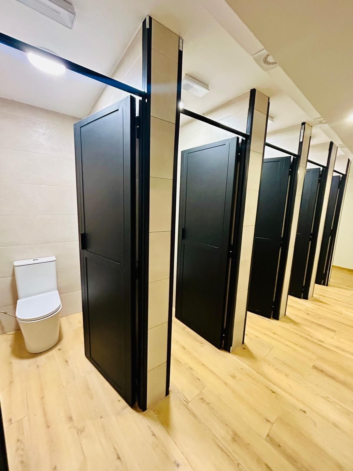 A row of black partitioned toilet stalls with a white toilet to the left.