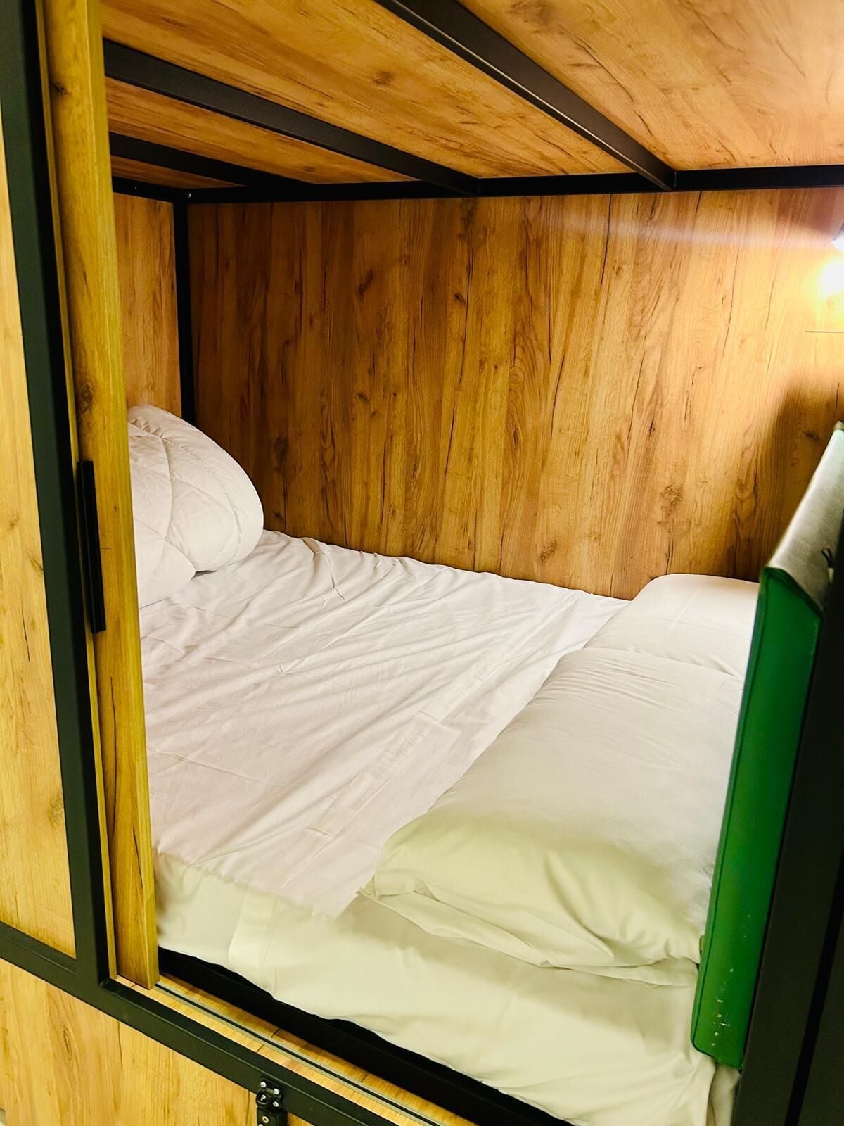 A small, enclosed wooden room with a single bed, a green chair, and a wooden ceiling.