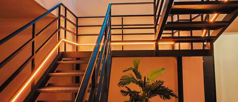 A modern staircase with metal railings and wooden steps, a neon sign reading "URBAN INN MADRID", and a potted plant in the center.