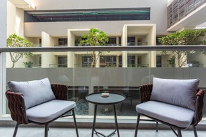 Een balkon met twee comfortabele stoelen en een kleine ronde tafel, met uitzicht op een gebouw met meerdere verdiepingen en groen.