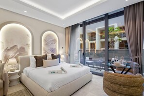 A modern hotel room with a large bed, a glass table with a view, and a balcony with outdoor seating.