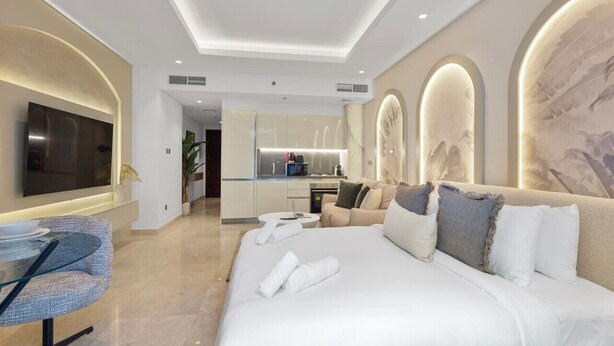 Een moderne hotelkamer met een groot bed, een televisie, een zithoek en een keuken op de achtergrond.