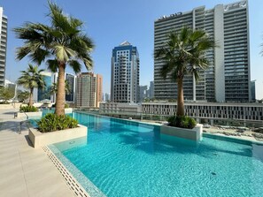 A rooftop swimming pool with palm trees, surrounded by high-rise buildings.