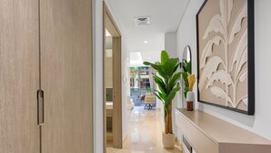 Een moderne hal met een houten deur, een potplant, een spiegel aan de muur en een decoratief paneel.