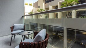 Een modern buitgedeelte met een glazen balustrade, twee comfortabele stoelen en een kleine ronde tafel.