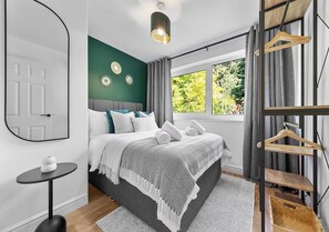 A modern bedroom with a bed, a bedside table, a mirror, and a window with curtains. - 2BR Flat, Free Parking, Close to Airport & Centre (Luton)