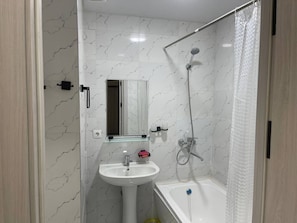 Un baño moderno con salpicadero de mármol blanco, un lavamanos, un espejo, una ducha y una bañera.