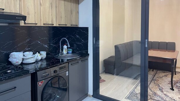 A modern kitchen with a built-in washing machine, a sink, and a dining area with a table and chairs. - Chaqar 317 (Tashkent)