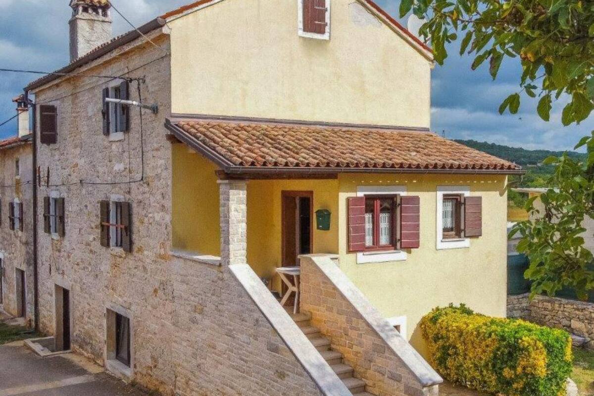 A two-story building with a stone facade, a tiled roof, and a small porch with a staircase leading to the entrance.