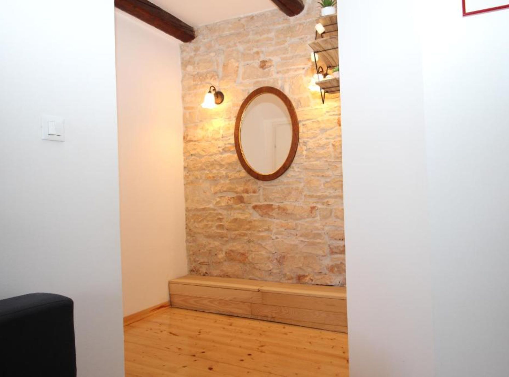 Ein Zimmer mit einer Steinwand, einer hölzernen Bank, einem runden Spiegel und einem kleinen Regal mit Dekoration.