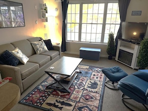 Una sala de estar con sofá, mesa de centro, alfombra estampada y televisor.