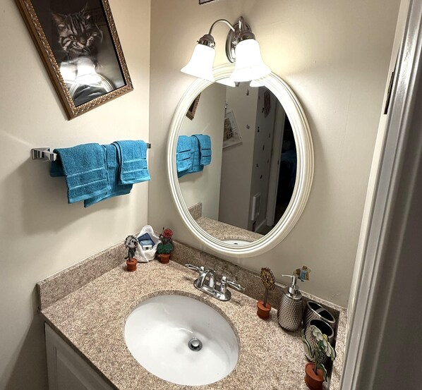 A bathroom with a round mirror, two blue towels, a sink, and a framed photo on the wall.