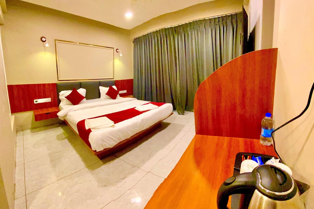 A hotel room with a bed, a desk with a kettle, a water bottle, and a curtain.