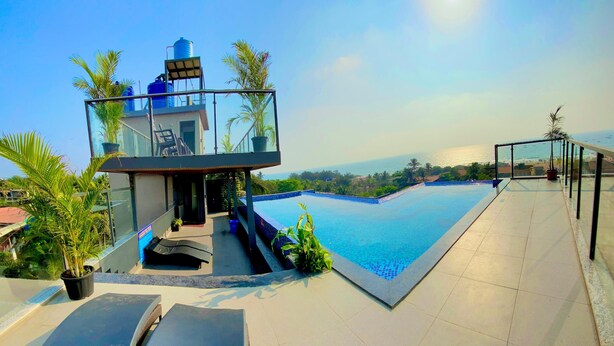 A rooftop pool with a clear view of the ocean, a glass-enclosed structure, and a few potted plants. - acanoa (Calangute)