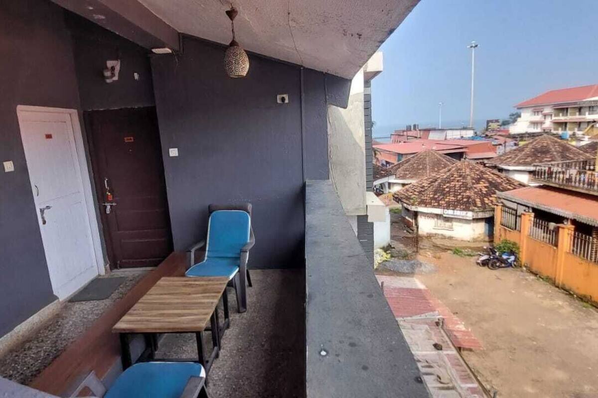 A balcony with a wooden table and two blue chairs, overlooking a residential area with houses and a parked motorcycle.