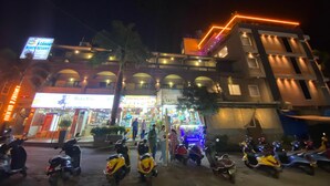 A building with multiple floors, a sign for a beach resort, and several shops with illuminated signs. - acanoa (Calangute)