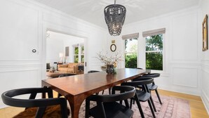 Comedor con mesa de madera, sillas negras, paredes blancas y una araña.