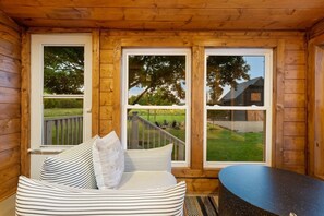 Une cabane en bois avec un canapé et une table, de grandes fenêtres donnant sur une cour verdoyante et un bâtiment.
