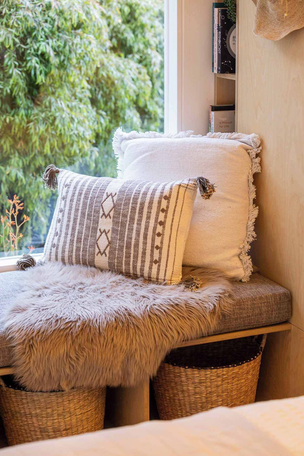 A cozy seating area with a bench, two patterned pillows, and a fur throw.