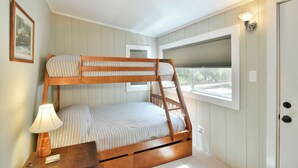 Un lit superposé avec une échelle, une lampe de chevet et une fenêtre avec des stores.