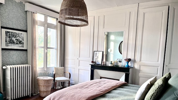 Un dormitorio con cama, una silla, tocador, espejo y ventana.