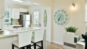A modern kitchen with white cabinetry, a stainless steel refrigerator, a dining table with white chairs, and a wall clock. - 4 Homes in downtown Mt. Shasta sleeps 24!! (Mt. Shasta)