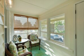 A sunroom with wicker furniture, a small table, and a view of the street outside.