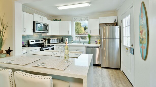 A modern kitchen with white cabinets, stainless steel appliances, and a dining area with a white table and chairs. - 4 Homes in downtown Mt. Shasta sleeps 24!! (Mt. Shasta)