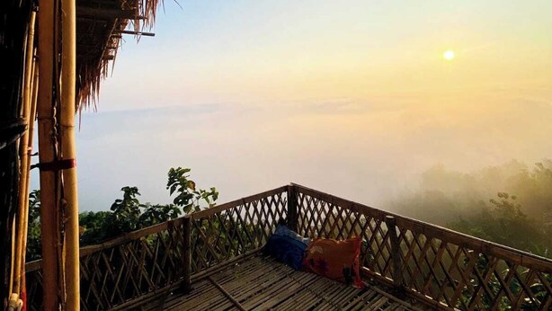 Une structure en bambou surmontée d’un toit de chaume, offrant une vue sur un paysage brumeux.