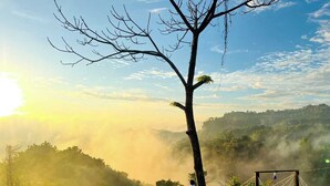 Une personne est assise sur une plateforme en bois, d’où l’on peut admirer un paysage brumeux et un ciel dégagé.