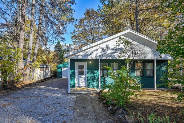 A small, single-story building with a gabled roof, surrounded by trees and a gravel path.