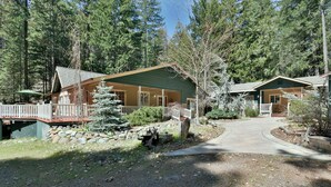A lodge with a covered deck, stone pathway, and forested surroundings. - Shasta Cottage, A romantic get-away in Mt. Shasta. (Mt. Shasta)