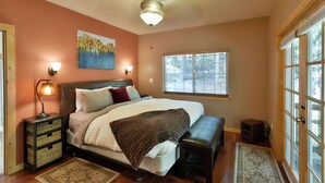 A bedroom with a bed, bedside lamps, a ceiling fan, a window with blinds, and a door with glass panels. - Shasta Cottage, A romantic get-away in Mt. Shasta. (Mt. Shasta)