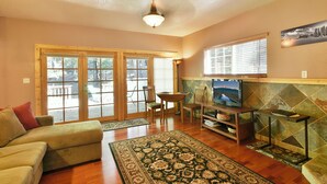 A living room with a sofa, a TV, a fireplace, and a large window. - Shasta Cottage, A romantic get-away in Mt. Shasta. (Mt. Shasta)