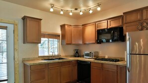 A kitchen with wooden cabinets, a microwave, a toaster, a refrigerator, and a window with blinds. - Shasta Cottage, A romantic get-away in Mt. Shasta. (Mt. Shasta)