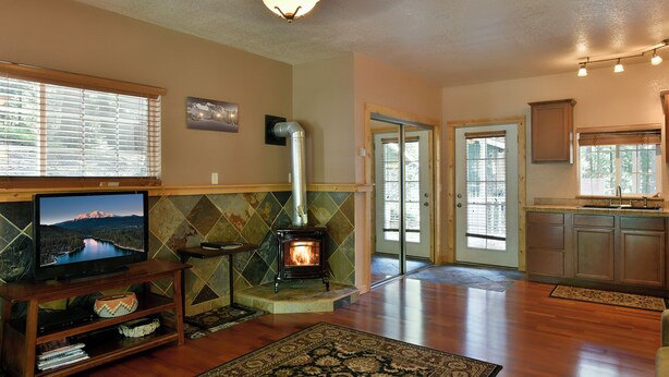 A living room with a fireplace, a television, and a kitchen area. - Shasta Cottage, A romantic get-away in Mt. Shasta. (Mt. Shasta)