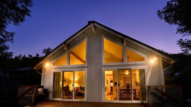 Une maison à deux étages avec de grandes fenêtres et une terrasse en bois.