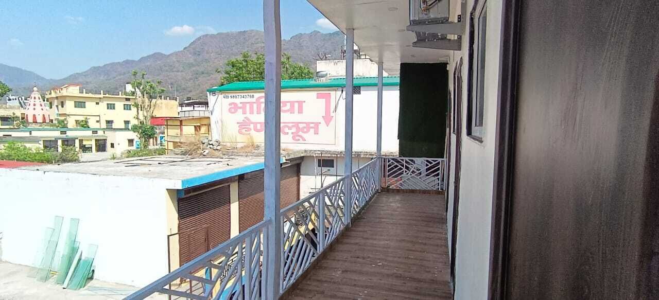 A balcony with a metal railing overlooking a street with buildings and mountains in the background.