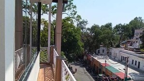A balcony with a wooden floor and white railings, overlooking a street with buildings and parked cars. - Hotel The Shivraat (Rishikesh)