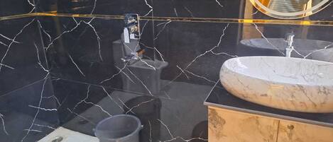 Un baño con salpicadero de mármol negro, un lavabo blanco y un mueble de tocador de madera.