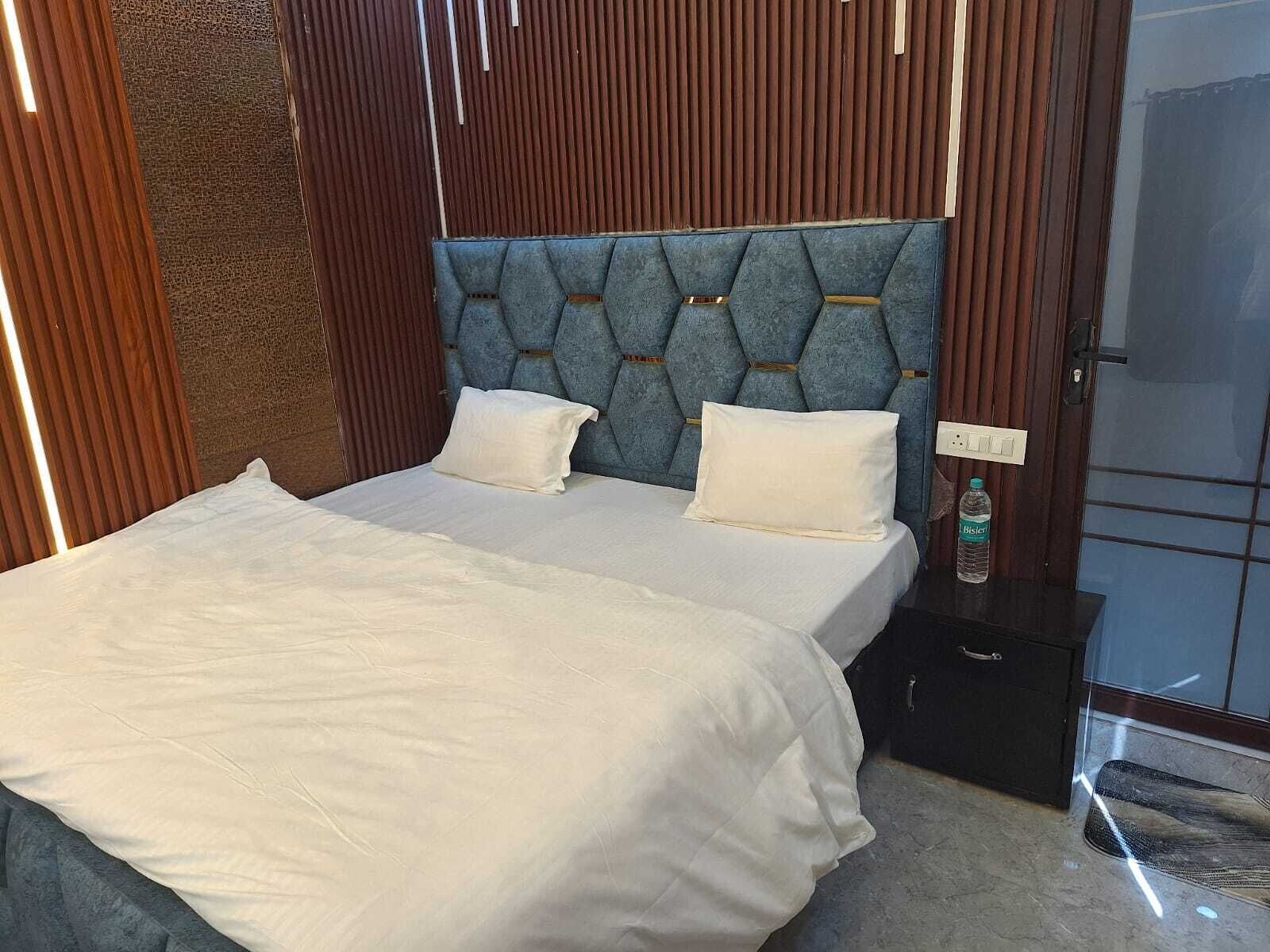 A modern bedroom with a tufted headboard, two white pillows, a neatly made bed, a bedside table with a bottle, and a nightstand.