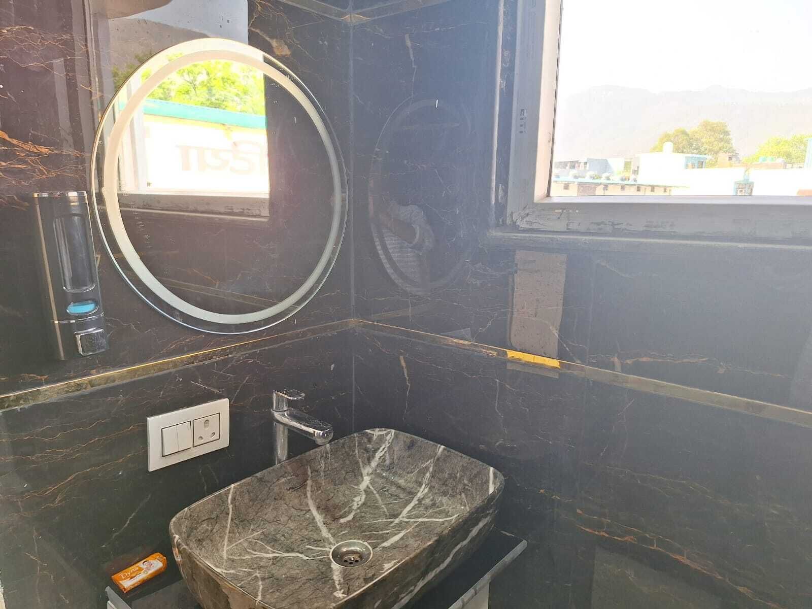 A bathroom with a marble sink, a round mirror, and a window with a view of buildings.