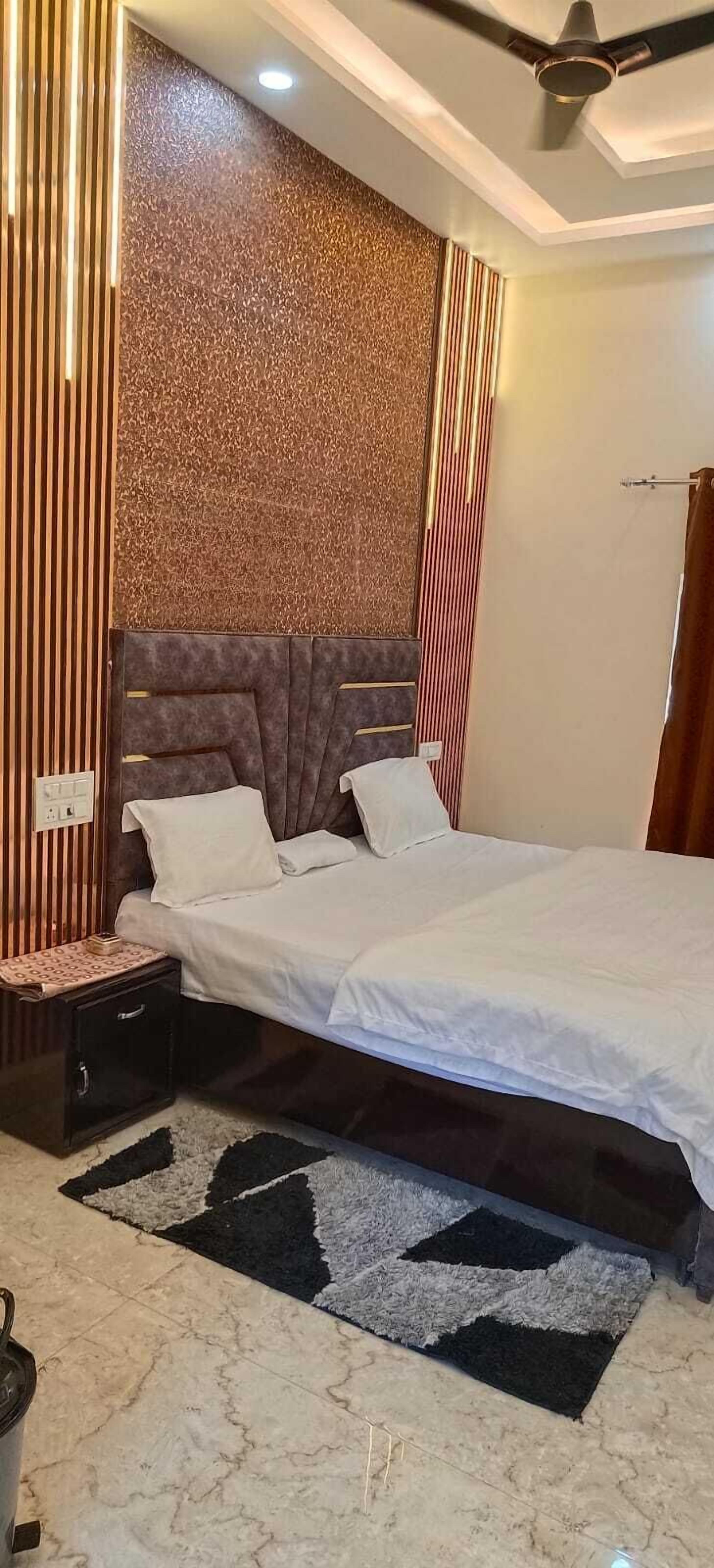 A modern bedroom with a large bed, a headboard with a textured pattern, a nightstand, and a black and white rug.