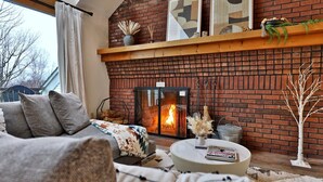 Ein gemütliches Wohnzimmer mit Kamin aus Ziegelsteinen, einer Couch, einem runden Couchtisch und einem Bücherregal mit Dekoration.