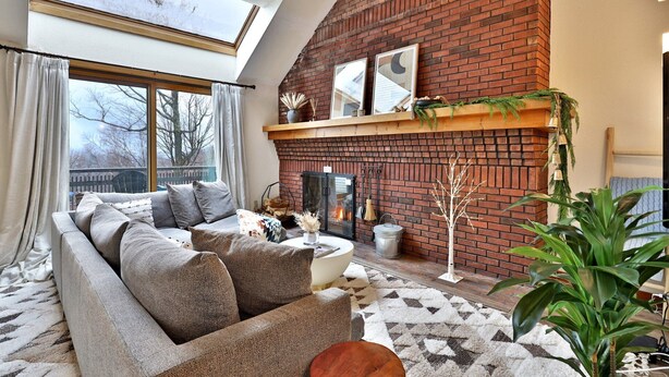Ein Wohnzimmer mit Kamin aus Ziegeln, einer Couch, einem runden Couchtisch und einem großen Fenster mit Vorhängen.