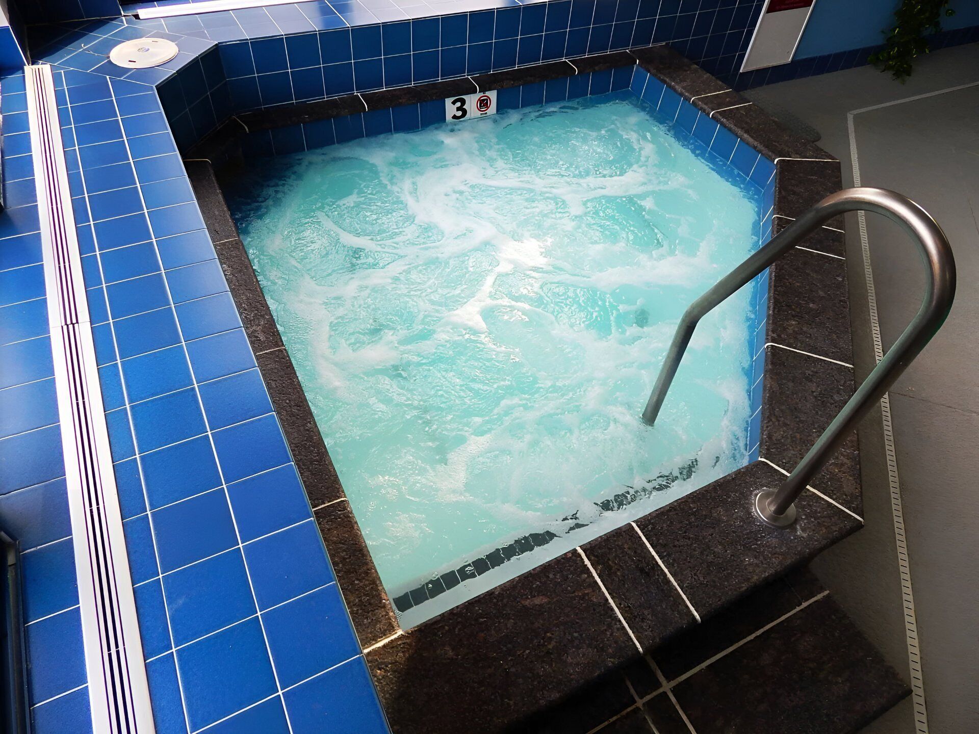 Ein Whirlpool mit blauen Fliesen und einer Metallhandstange.