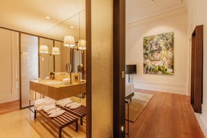 A modern bathroom with a large mirror, dual sinks, and a bench with towels.
