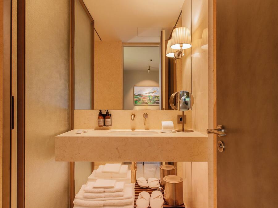 A modern bathroom with a large mirror, a sink, and a shelf with towels.